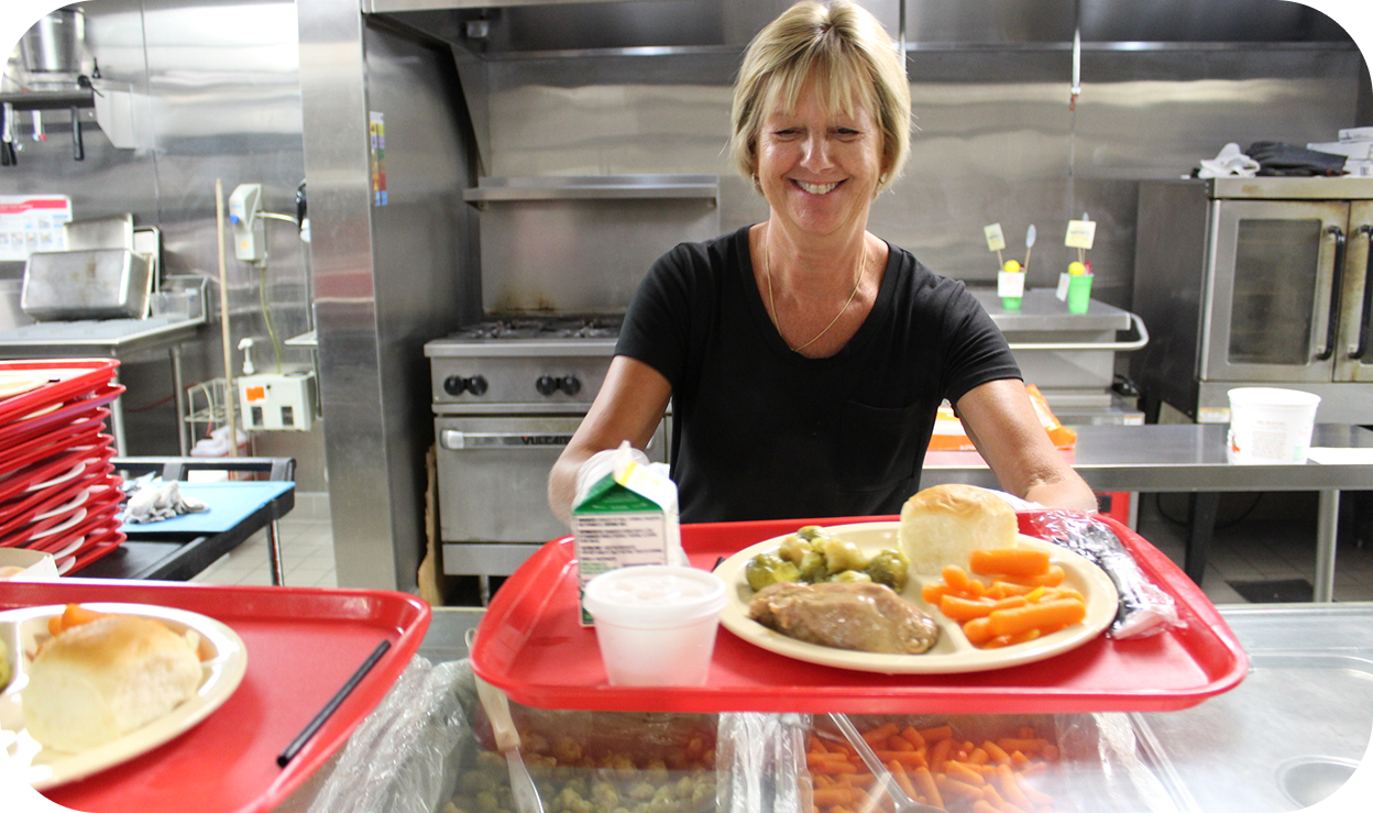 A woman serving a platter of food in a dining hall