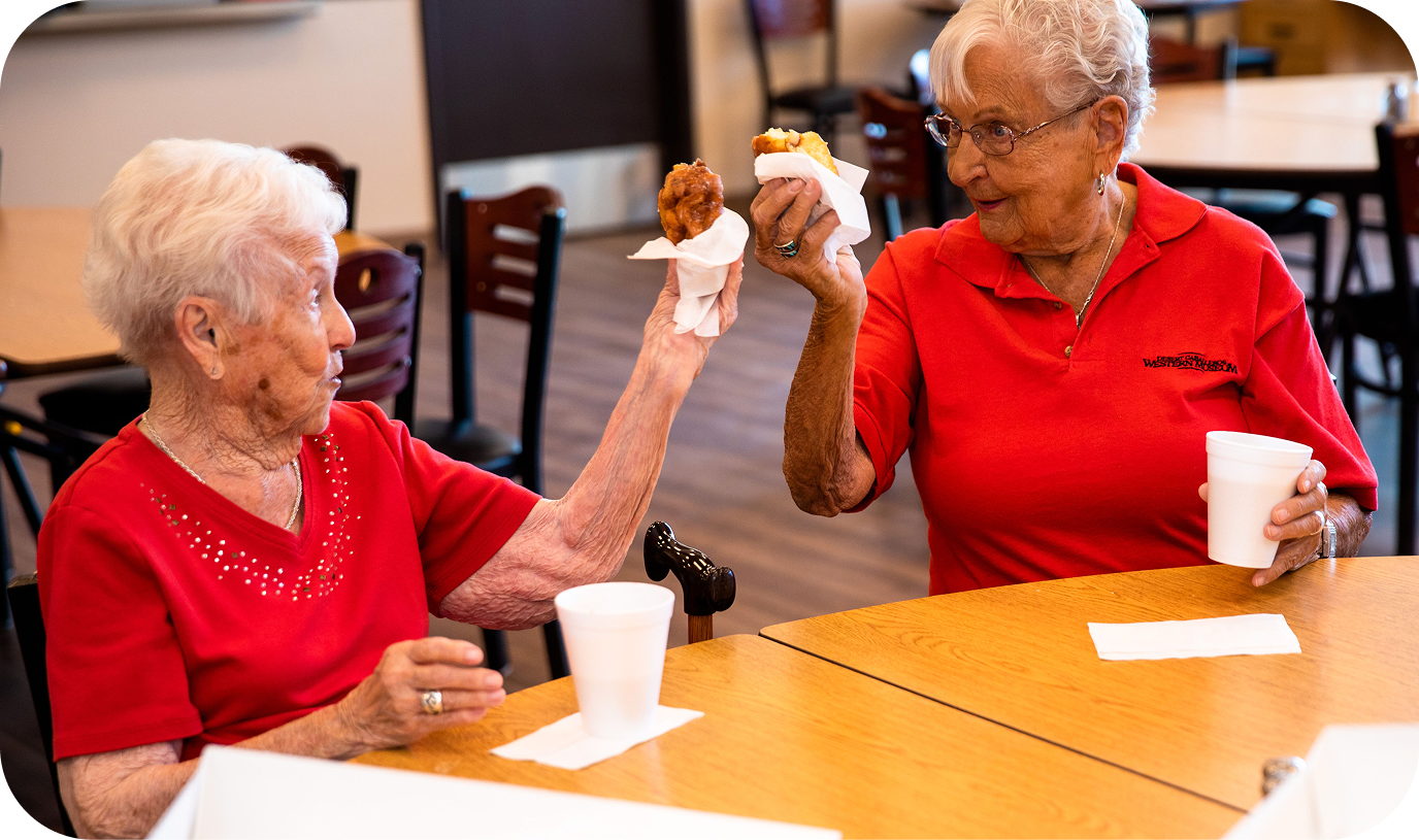 Two elderly women who are friends sharing a snack with one another