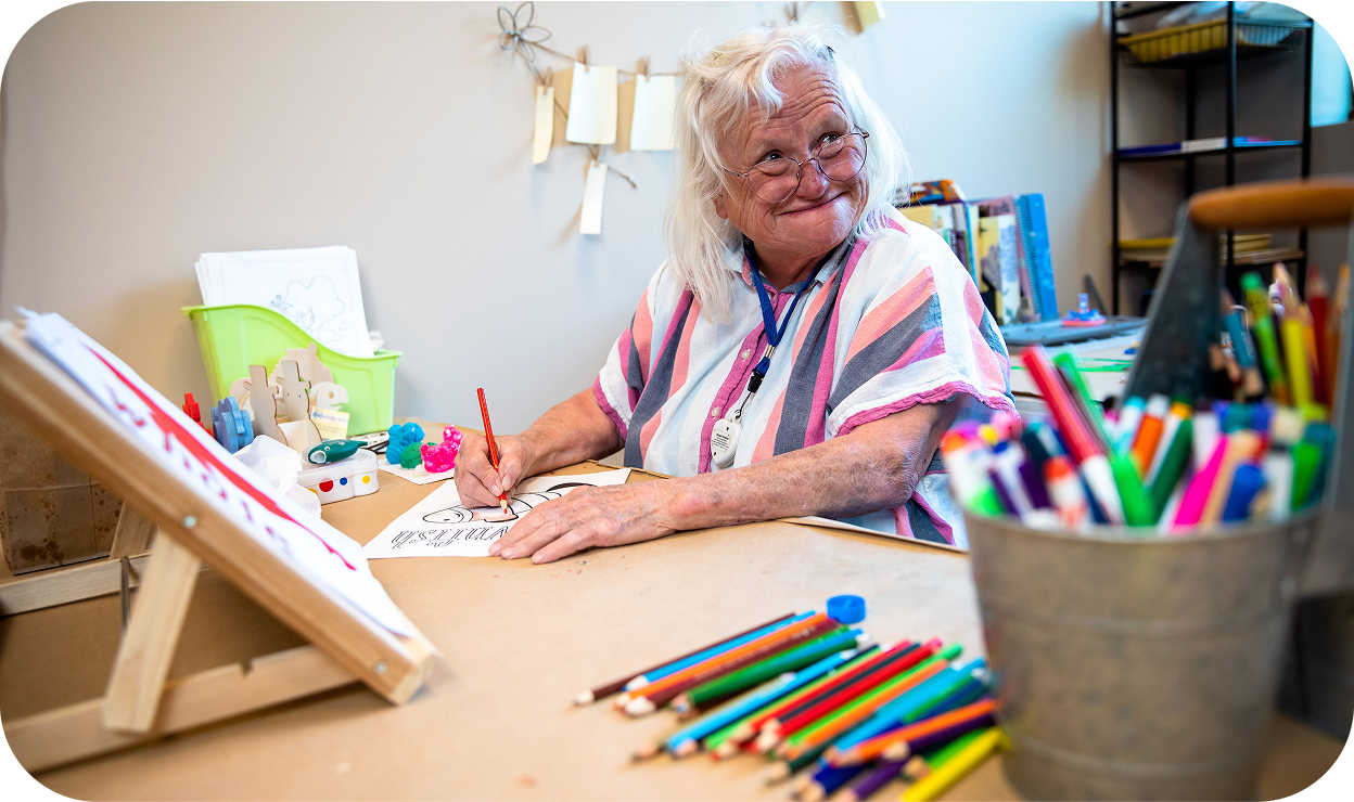 An elderly woman filling in coloring pages with color pencil with a big smile
